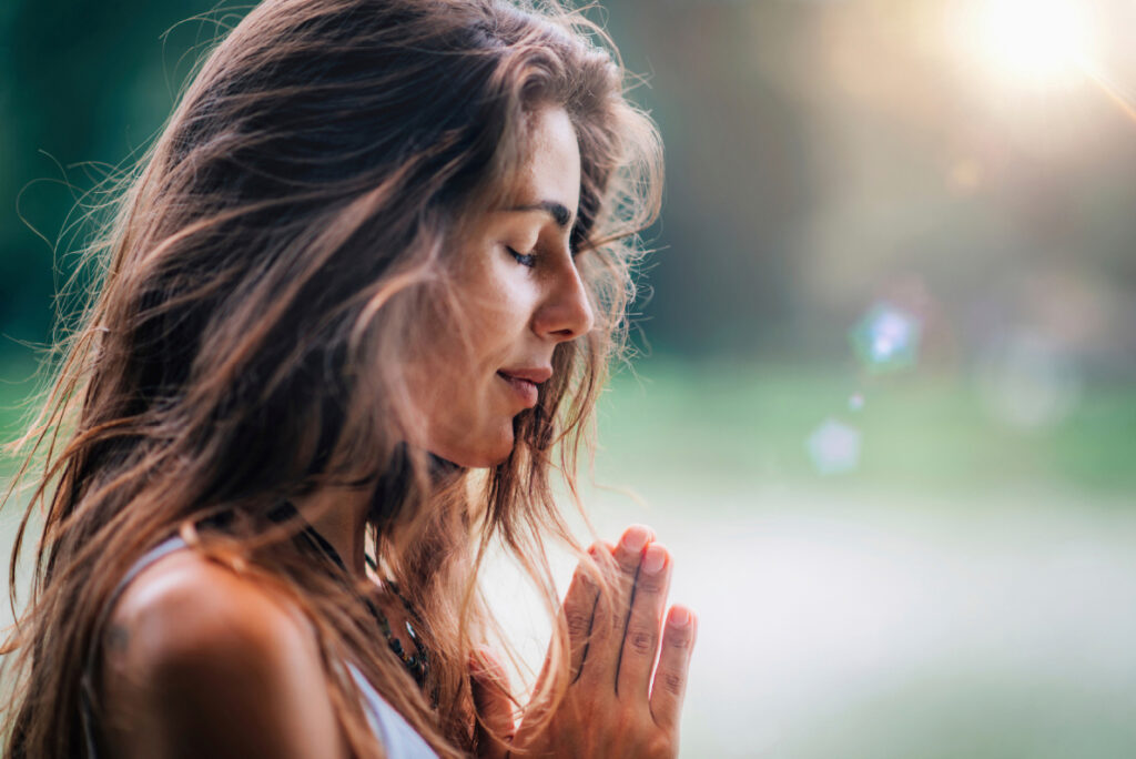 Woman meditating with hands in prayer - The Ophiuchus Healing Center